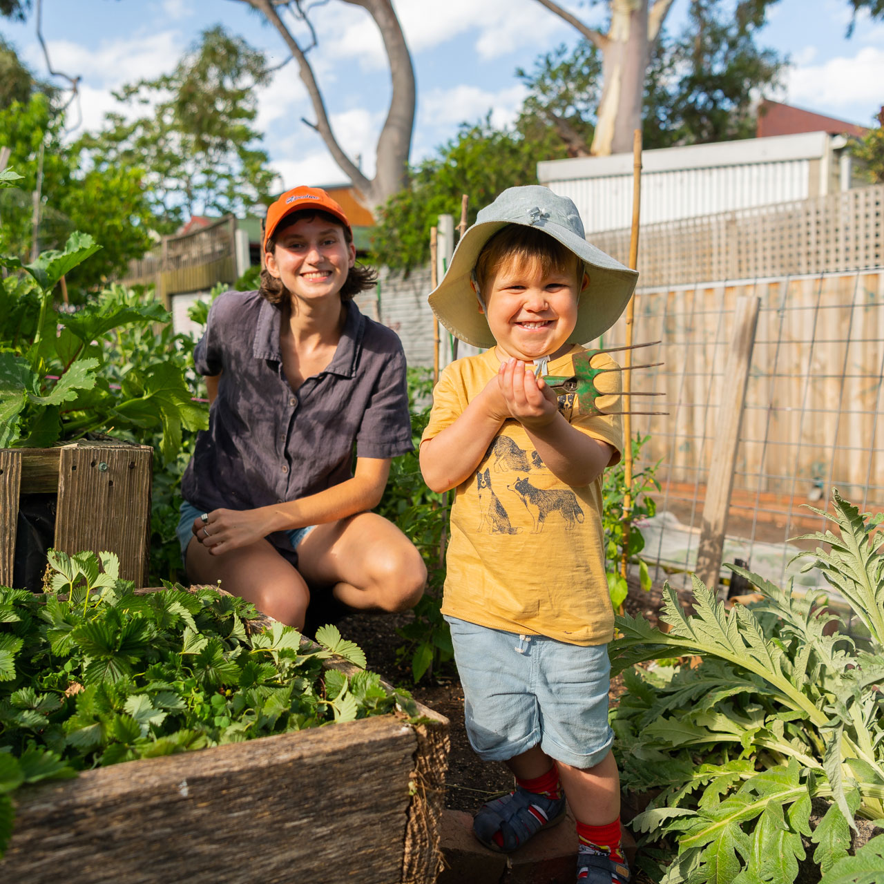 Image of a child holding a trowel and a younger person in a vegetable garden