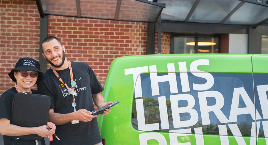 Two members of staff are holding iPads next to the Yarra Libraries van.